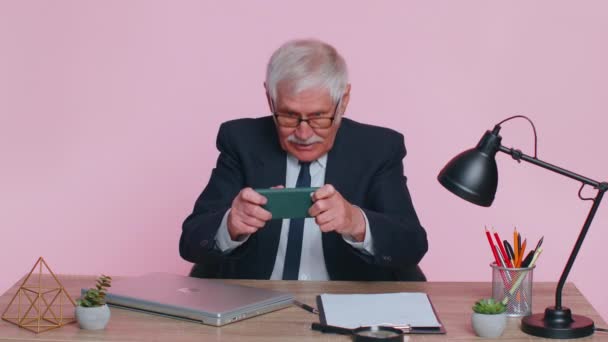 Занепокоєний старший бізнесмен сидить на робочому місці, уникаючи роботи та гри в гонки або шутер відеоігри — стокове відео