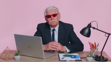 Kıdemli iş adamı onaylıyor, onaylıyor, onaylıyor, pembe ofisteki bilgisayarı kullanarak iyi haberleri seviyor.