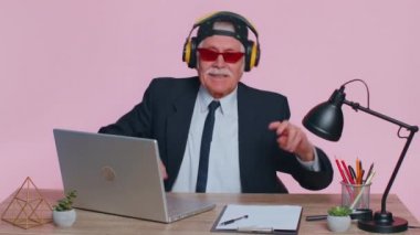 Senior old business man listening music on headphones, dancing disco fooling around, celebrating win