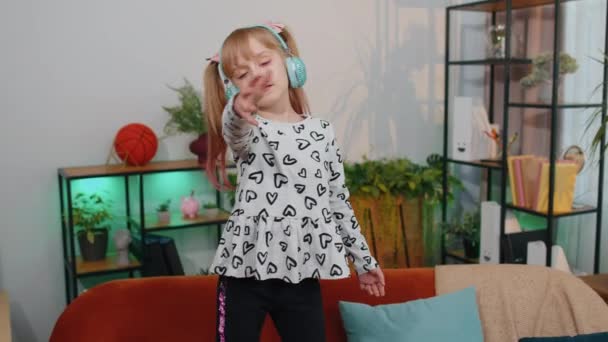 Happy child girl kid in headphones dancing and jumping while listening to the music at home alone — Stock Video