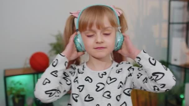 Criança feliz menina criança em fones de ouvido dançando e pulando enquanto ouve a música em casa sozinho — Vídeo de Stock