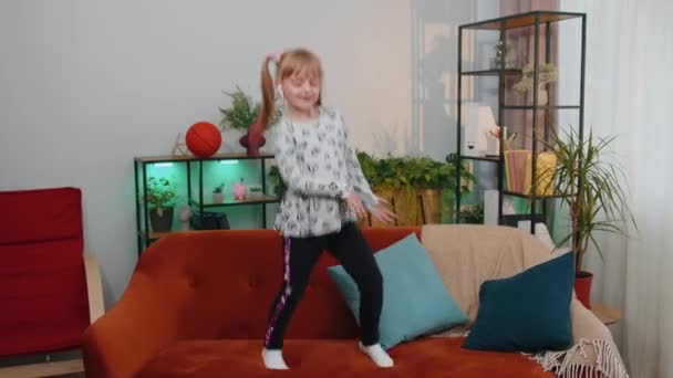 Criança feliz menina garoto usa fones de ouvido dançando e pulando enquanto ouve a música em casa sozinho — Vídeo de Stock