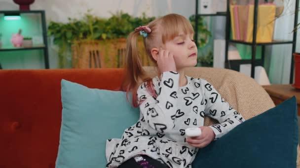 Little children girl relaxing on sofa, wearing wireless earphones, listening to music, favorite song — стоковое видео