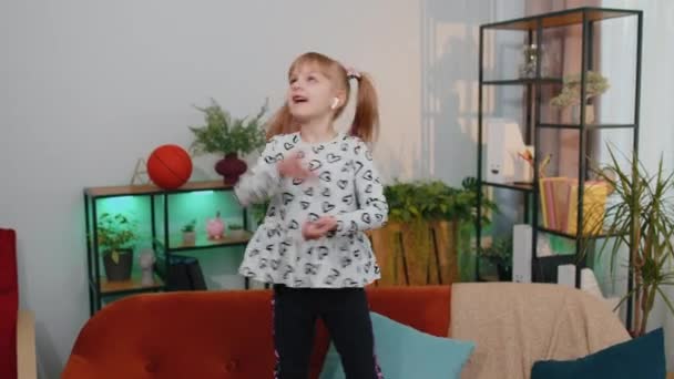 Šťastné dítě dívka nosí sluchátka tanec a skákání při poslechu hudby doma sám — Stock video