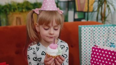 Young little children girl sitting on sofa with lots of gifts celebrating birthday party anniversary