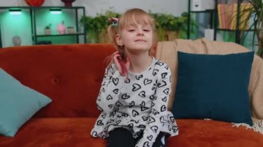 Cheerful lovely caucasian little toddler kid girl smiling, looking at camera sitting on sofa at home