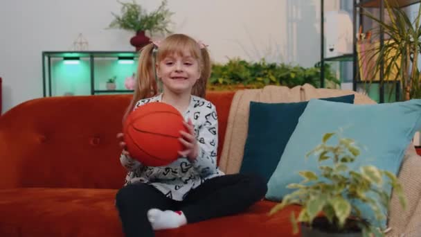 Malé děti dívka basketbalový fanoušek drží míč při pohledu na kameru, trénink dribling doma — Stock video