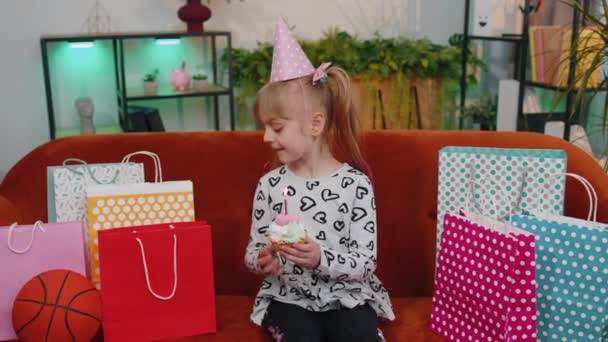 Happy child girl with lots of gifts celebrating birthday party making a wish, blowing cake candle — Vídeos de Stock