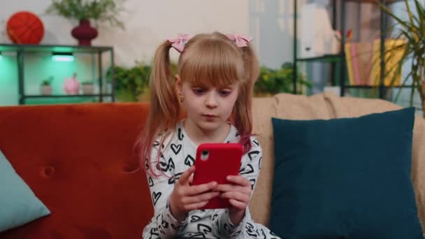 Захоплена здивована дівчинка-переможець використовує мобільний телефон, скажімо, вау так, піднімаючи руки в несподіваному стані один вдома — стокове відео