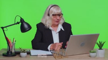 Senior businesswoman in headphones making conference video call on laptop call center agent operator