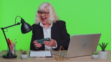 Worried senior businesswoman sits at workplace avoid working, playing racing or shooter video games