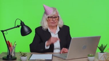 Sad upset lonely senior businesswoman celebrating birthday party alone, holds cake at green office