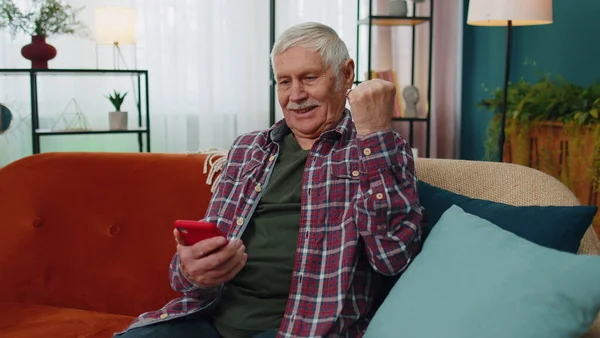 Overjoyed starszy dziadek człowiek trzymać smartfon, podekscytowany aplikacji mobilnej sportowej licytacji wygrać zakład w domu — Zdjęcie stockowe