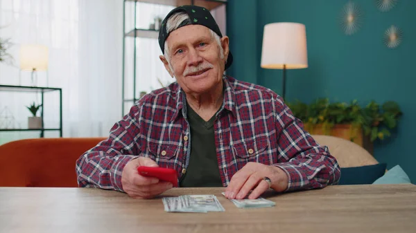 Smiling senior man holding money cash and smartphone, satisfied of income, planning family budget — Stock Photo, Image