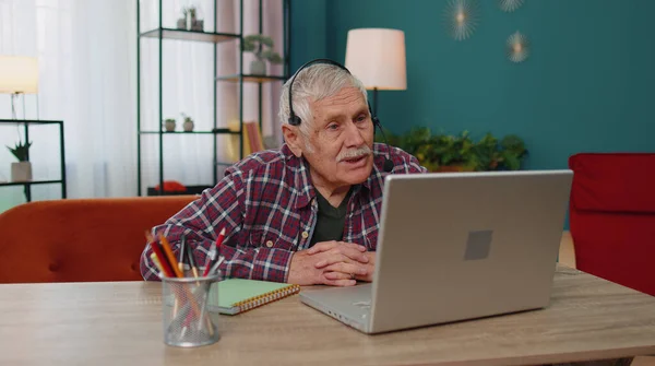 Senior mężczyzna freelance nosić słuchawki nawiązać rozmowę wideo, nauczanie na laptopie w biurze domu — Zdjęcie stockowe