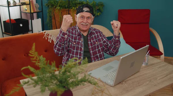 Grandfather man playing computer video games on laptop computer, wins, celebrate, smiles happily — стоковое фото