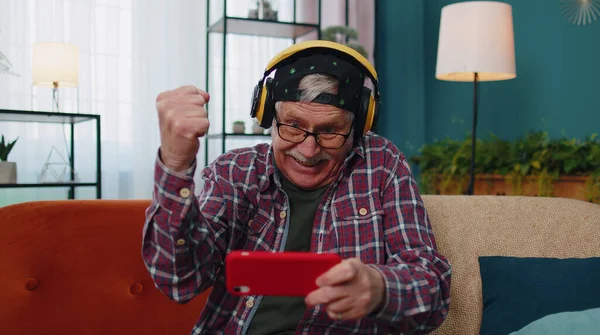 Preoccupato divertente anziano nonno uomo giocare sparatutto video giochi online sul telefono cellulare a casa — Foto Stock