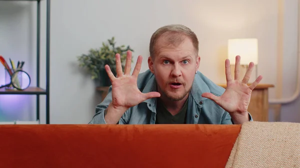 Man playing hide and seek peekaboo game hiding behind sofa looking at camera, positive smiling