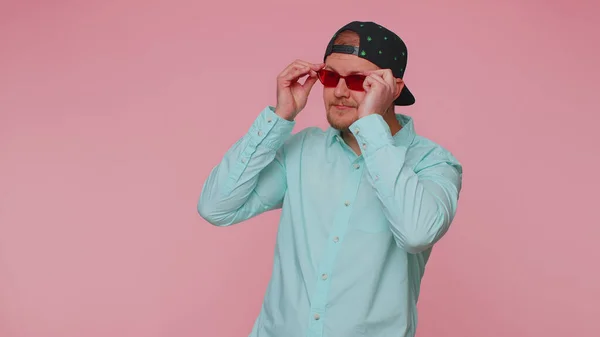 Seductor hombre elegante alegre en camisa azul con gafas de sol, sonrisa encantadora en la pared rosa — Foto de Stock