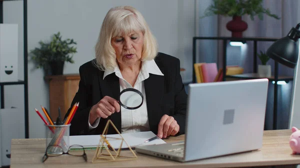 Senior donna d'affari guarda attraverso una lente d'ingrandimento, indagare, analizzare, leggere documenti — Foto Stock