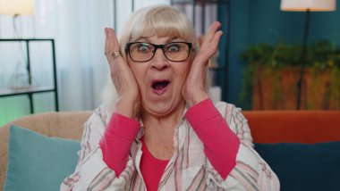 Vay canına, heyacanlı yaşlı büyükanne büyük gözleriyle kameraya bakarken şaşkınlıkla el kaldırıyor.