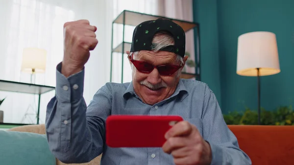 Preoccupato divertente anziano nonno uomo giocare sparatutto video giochi online sul telefono cellulare a casa — Foto Stock