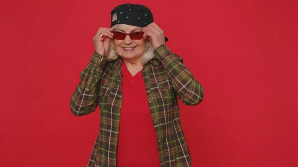 Séduisante vieille femme élégante et gaie en chemise portant des lunettes de soleil, sourire charmant sur le mur rose — Photo