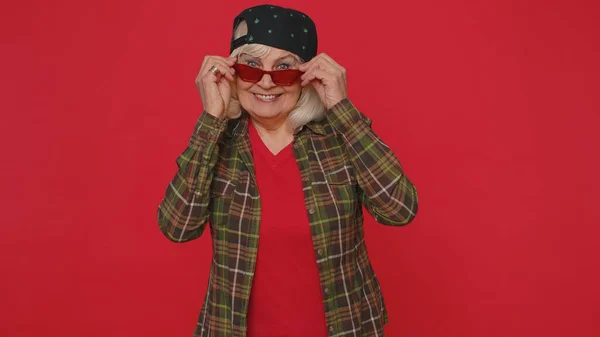 Séduisante gaie élégante vieille femme mature en chemise portant des lunettes de soleil, sourire charmant sur le mur rose — Photo