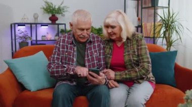 Çok mutlu, yaşlı bir aile çifti, büyükanne ve büyükbaba. Akıllı telefon sahibi kadın, mobil uygulama spor bahsi kazanacağı için heyecanlı. Mutlu büyükanne büyükbaba zaferi kutluyor.