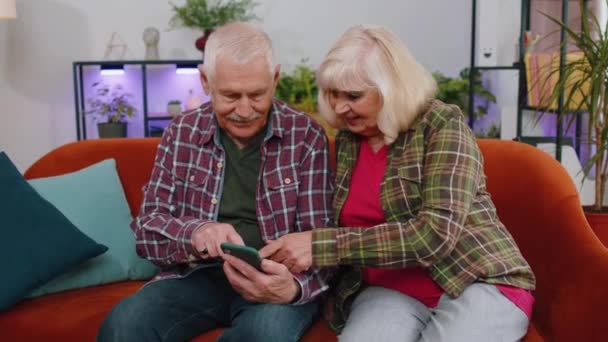 うわぁ 素晴らしい高齢者の家族のカップル祖父母の男性の女性は 携帯電話のスマートフォンを使用し 良いニュースメッセージを受信し 突然の勝利にショックを受け 勝利を祝い 自宅でオンラインショッピングを購入 — ストック動画