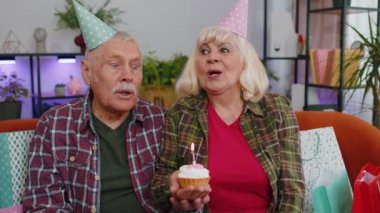 Mutlu son sınıf aile çifti büyükanne ve büyükbaba kadın şenlikli doğum günü şapkası takıyor ve kekin üzerinde mum yakma yıldönümünü kutluyor. Büyükanne dedemin evde hediyeleri var.