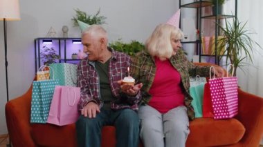 Mutlu son sınıf aile çifti büyükanne ve büyükbaba kadın şenlikli doğum günü şapkası takıyor ve kekin üzerinde mum yakma yıldönümünü kutluyor. Büyükanne dedemin evde hediyeleri var.