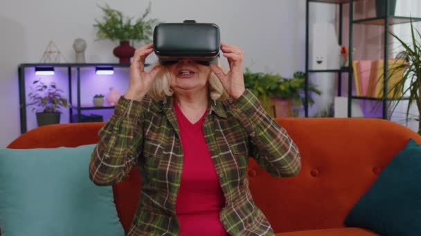 ヘッドセットヘルメットアプリを使用してシミュレーションゲーム シミュレーションメガネガジェット技術を再生する高齢者の女性 仮想現実3D 360ビデオを見る 熟女祖母でVrゴーグル上のソファ ホーム — ストック動画