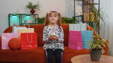 Kanepede bir sürü hediyeyle oturan küçük bir kız çocuğu evde yalnız başına doğum günü partisini kutluyor. Mutlu çocuk pasta tutuyor, dilek diliyor ve bir mum üflüyor.