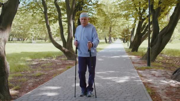 Senior zdrowy emeryt dziadek szkolenia nordic walking używać kijki trekkingowe w parku letnim — Wideo stockowe