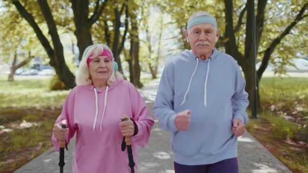 Vrolijk ouder stel grootvader, grootmoeder opleiding Nordic walking, hardlopen in het zomerpark — Stockvideo