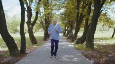 Motivasyonlu sporcu emekli yaşlı adam parkta koşuyor, büyükbabam nabzını kontrol ediyor.