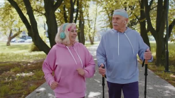 Aktywni starsi dziadkowie trenujący nordic walking z kijkami trekkingowymi, biegający w letnim parku — Wideo stockowe