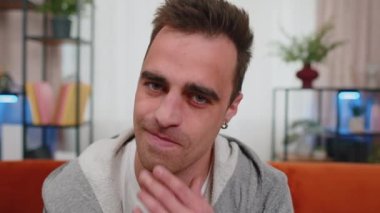 Mutlu, tıraşsız, sıradan tişörtlü, gülümseyen ve kameraya bakan bir gencin yakın portresi. Evde, oturma odasında, kanepede izole edilmiş genç bir model. Erkek doğası güzelliği