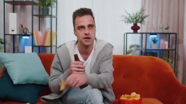 Kanepede oturan, cips yiyen, bira içen ve ilginç TV dizileri, futbol şampiyonası maçları, evdeki sosyal medya içerikleri izleyen bir adamın portresi. Ev eğlencesi seven adam.