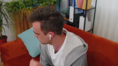 Telsiz kulaklıklara dokunan mutlu genç adam favori enerjik disko müziğini seçiyor dinlenen, dinlenen, dinlenen, evdeki kanepede uzanan şarkılar dinliyor. Hafta sonları evde eğlenceli aktiviteler