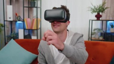 VR kulaklık takan heyecanlı bir adam oturma odasında koltukta tek başına oturup fütürist teknoloji kullanarak el hareketleriyle 3 boyutlu video oyunu oynuyor. Sanal gerçeklik gözlükleri