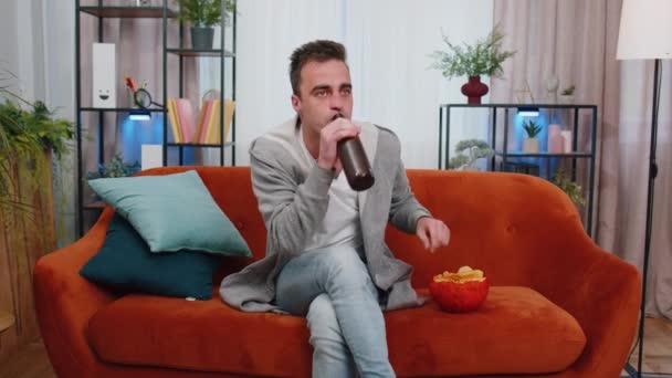 Podekscytowany Młodzieniec Siedzący Kanapie Jedzący Frytki Pijący Piwo Oglądający Ciekawy — Wideo stockowe