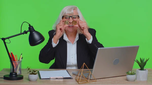Elderly old business woman showing golden bitcoins. Achievement career wealth, cryptocurrency investment mining money income future technology. Senior woman freelancer fooling, making faces at office