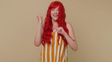 Çizgili kolsuz tişörtlü mutlu bir kadın bağırıyor, el kol hareketi yapıyor başarıyı kutluyor, kazanıyor, doğum günü, piyango hedefine ulaşıyor. Bej renkli stüdyo arka planında küçük bir kız.