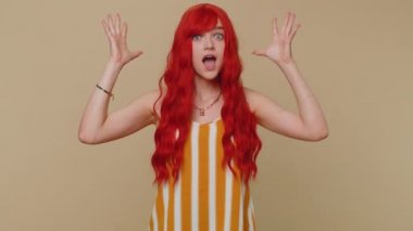 Aman Tanrım, vay canına. Heyecanlı kazanan kızıl saçlı kadın büyük gözleriyle kameraya bakarken şaşkınlıkla ellerini kaldırıyor, ani zaferden şok oluyor. Samimi genç kız bej renkli stüdyo arka planında tek başına.