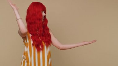 Güzel kızıl saçlı kadın boş bir yeri işaret ediyor ticari metinler için reklam alanı, ürün tanıtımı için fotokopi alanı. Genç kızıl kız. Bej arka planda kapalı stüdyo çekimleri