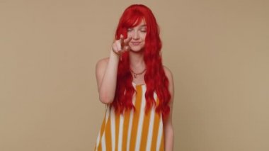 Gözüm üzerinde. Kolsuz tişörtlü kızıl kadın gözlerini ve kamerasını işaret ediyor. Seni jest yaparken, birini gözetlerken izlediğimi göster. Genç kızıl saçlı kız bej renkli stüdyo duvarında tek başına.