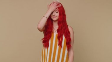 Üzgün, canı sıkkın kızıl bir kadın, el hareketi yapıyor, sıkılıyor, işten dolayı hayal kırıklığına uğruyor, kötü haber. Genç kızıl saçlı kız hayal kırıklığına uğramış, çaresiz yalnız başına bej rengi stüdyo arka planda.