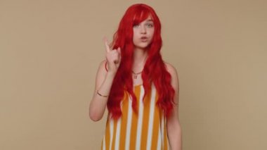 Memnun olmayan kadın parmağını sallar ve hayır der, dikkatli ol, tehlike hatasından kaçınmak için azarlar ve tavsiye verir, onaylamamak, itiraz işareti. Kızıl saçlı kız bej renkli stüdyoda tek başına izole edilmiş.